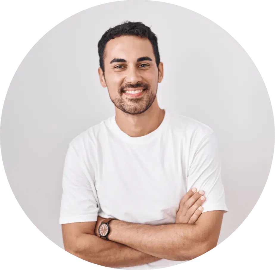 Smiling young man in a white t-shirt with arms crossed, expressing a relaxed and friendly demeanor.