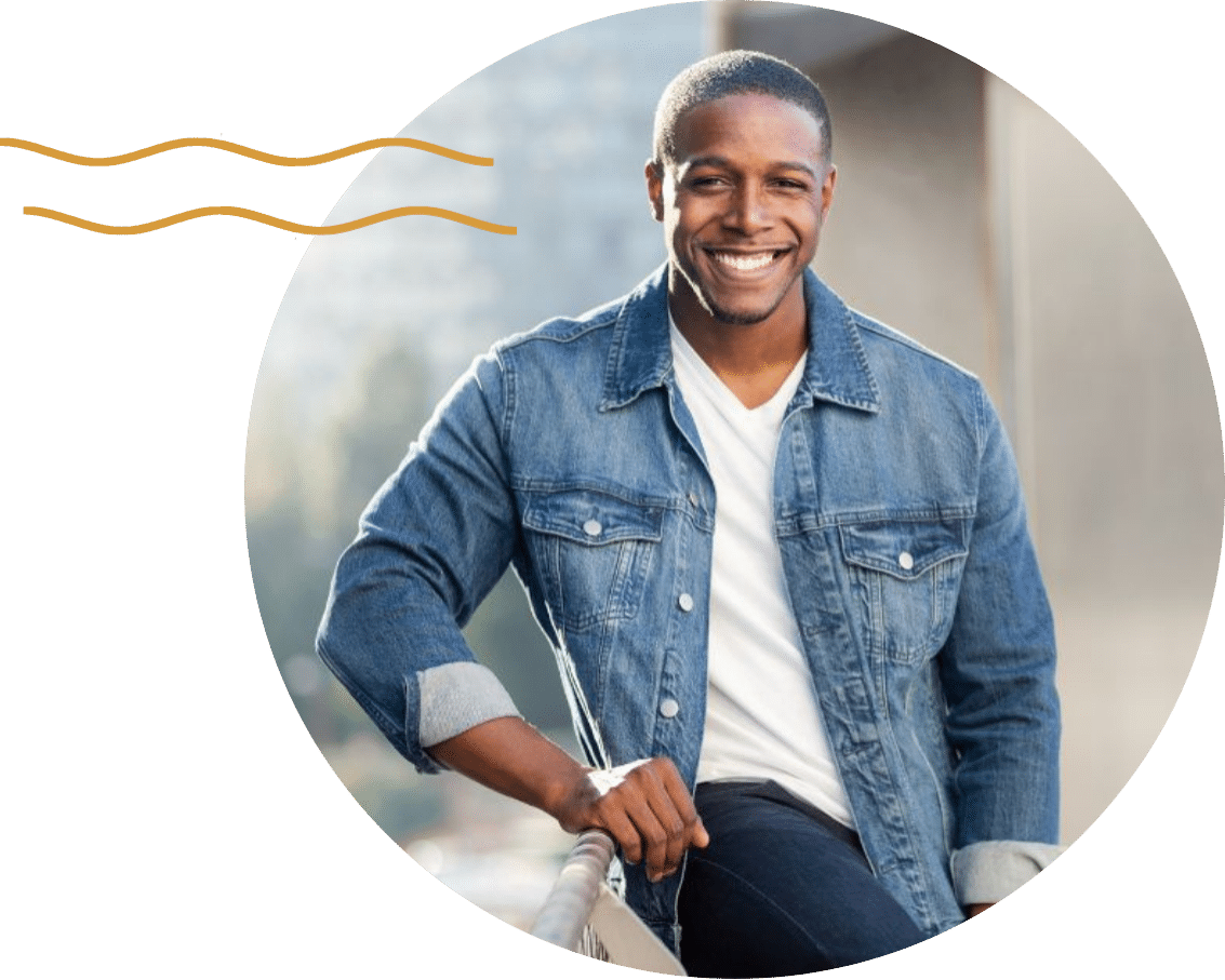 Veneers body image desktop A young man wearing a denim button-up standing against a rail and smiling