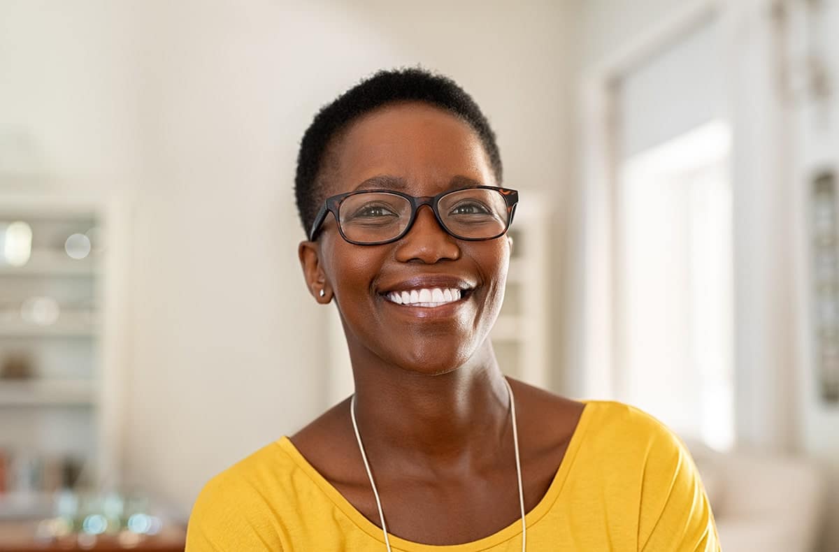 A middle-aged woman with short hair and glasses wearing a yellow shirt and smiling